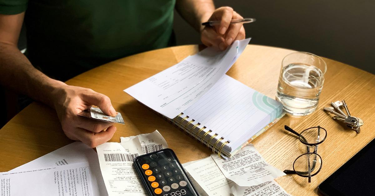 el hombre está haciendo una auditoría de los gastos domésticos usando una calculadora y un cuaderno